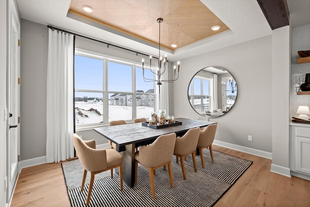 dining room with a raised ceiling, a notable chandelier, and light hardwood / wood-style floors