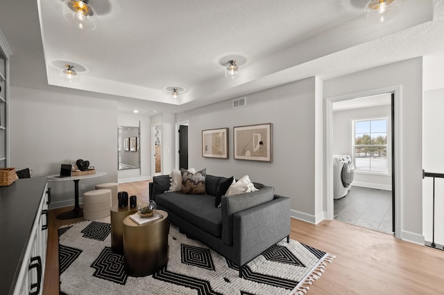 living room with a raised ceiling, washer and dryer, a textured ceiling, and light hardwood / wood-style floors