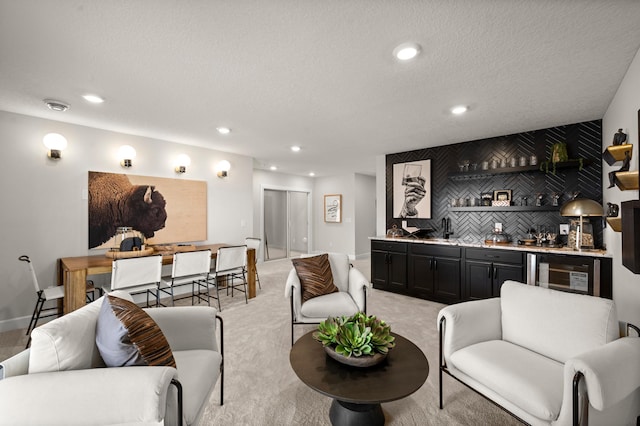 interior space with light colored carpet, a textured ceiling, beverage cooler, and indoor bar