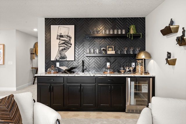 bar featuring sink, beverage cooler, backsplash, and light stone countertops