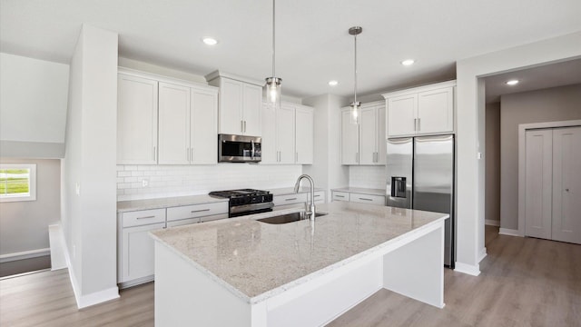 kitchen with a center island with sink, sink, hanging light fixtures, appliances with stainless steel finishes, and white cabinets