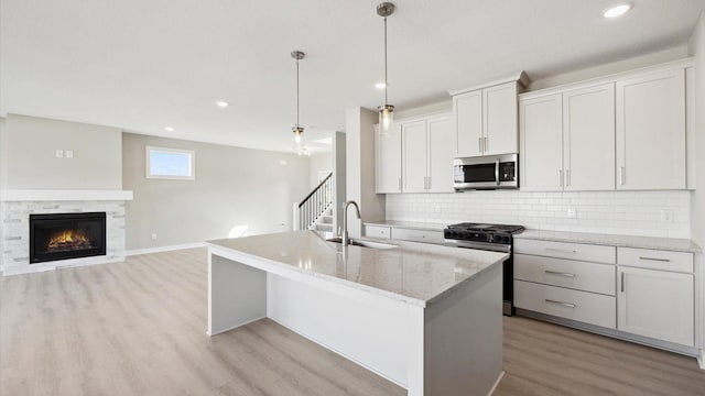 kitchen with white cabinets, decorative light fixtures, stainless steel appliances, sink, and a center island with sink