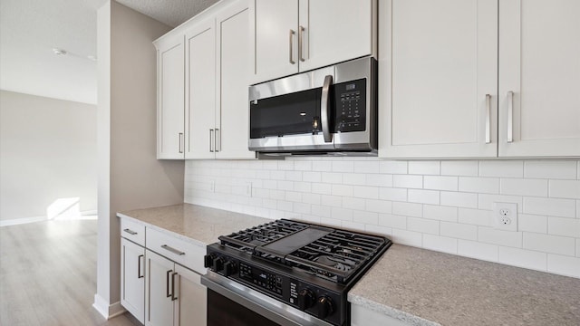 kitchen featuring light stone countertops, white cabinets, appliances with stainless steel finishes, decorative backsplash, and light wood-type flooring