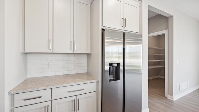 kitchen featuring white cabinetry, stainless steel fridge, decorative backsplash, light hardwood / wood-style flooring, and light stone counters