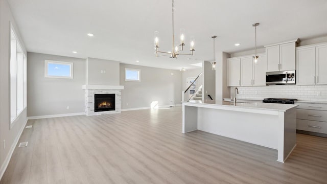 kitchen featuring white cabinetry, a center island with sink, tasteful backsplash, pendant lighting, and sink