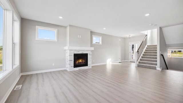 unfurnished living room with a stone fireplace and light wood-type flooring