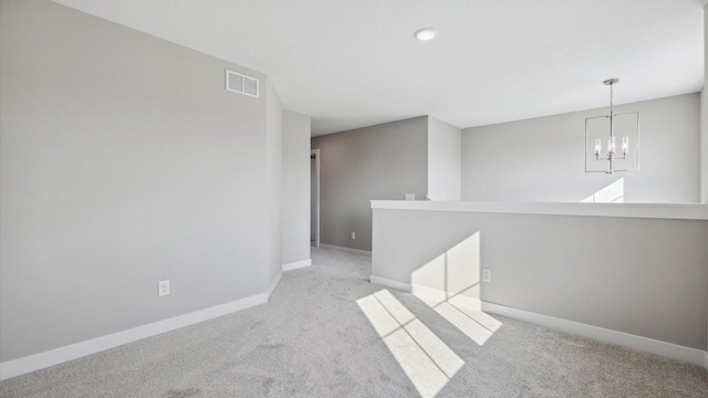 empty room with light colored carpet and a notable chandelier