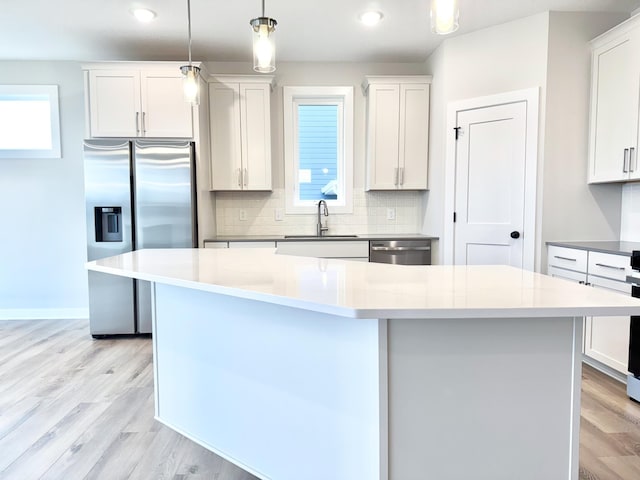 kitchen featuring pendant lighting, stainless steel appliances, a kitchen island, and white cabinets