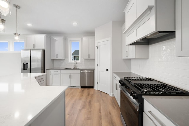 kitchen featuring sink, white cabinetry, appliances with stainless steel finishes, custom range hood, and pendant lighting