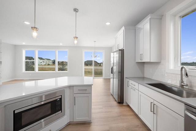 kitchen with sink, hanging light fixtures, stainless steel appliances, tasteful backsplash, and white cabinets