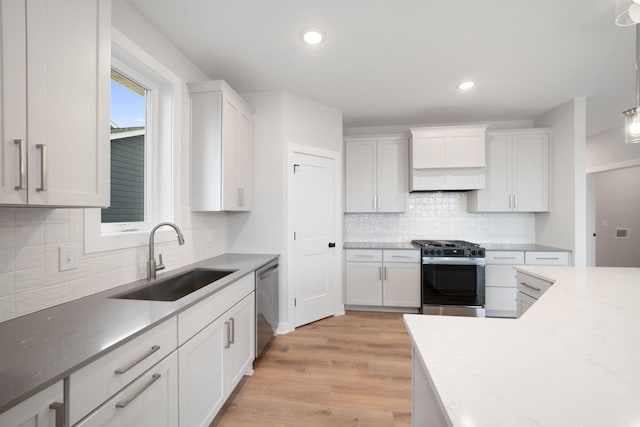 kitchen featuring sink, white cabinets, hanging light fixtures, stainless steel appliances, and light wood-type flooring