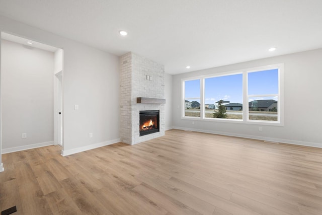 unfurnished living room with a brick fireplace and light hardwood / wood-style flooring