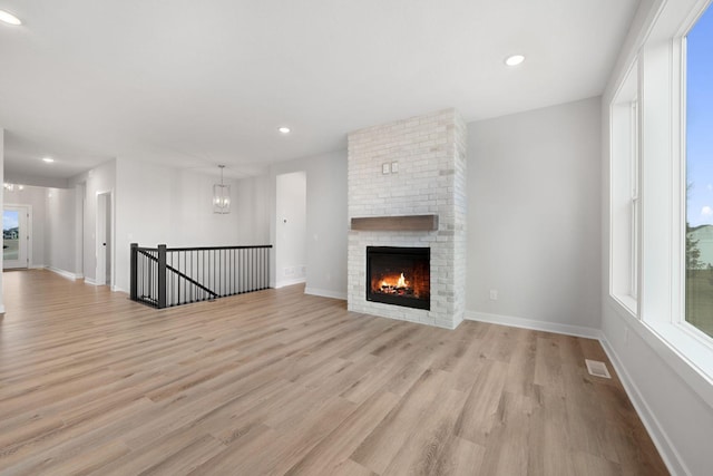 unfurnished living room with a brick fireplace, a chandelier, and light hardwood / wood-style flooring