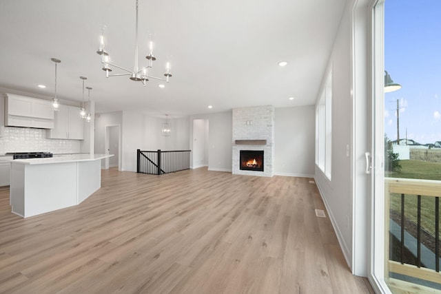 unfurnished living room with light hardwood / wood-style flooring, a notable chandelier, and a fireplace