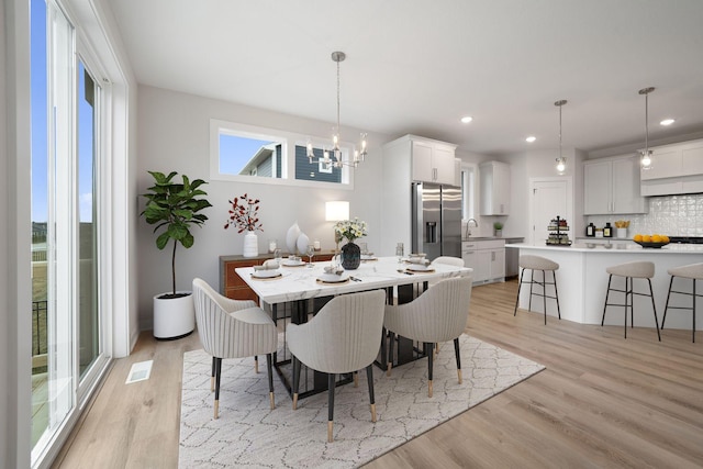 dining area featuring an inviting chandelier, sink, and light hardwood / wood-style flooring