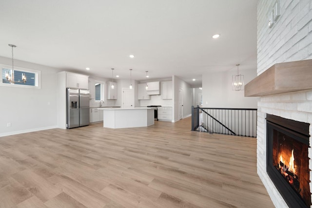 unfurnished living room featuring an inviting chandelier, sink, light hardwood / wood-style floors, and a large fireplace