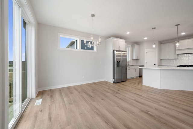 10142 Arrowwood Trl, Woodbury, MN 55129 - kitchen with stainless steel fridge, a chandelier, decorative backsplash, light countertops, and light wood-style floors