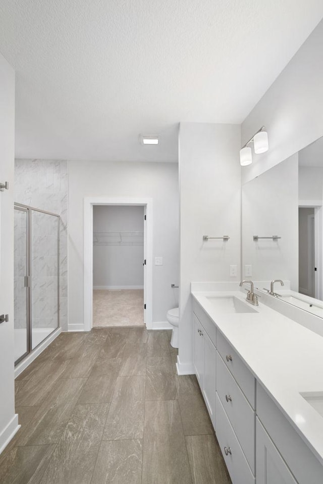 10142 Arrowwood Trl, Woodbury, MN 55129 - bathroom featuring a shower stall, toilet, double vanity, a walk in closet, and a textured ceiling
