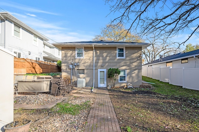 rear view of property with cooling unit and a hot tub