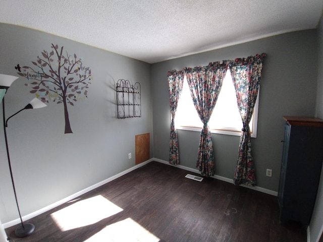 unfurnished room with baseboards, a textured ceiling, visible vents, and wood finished floors