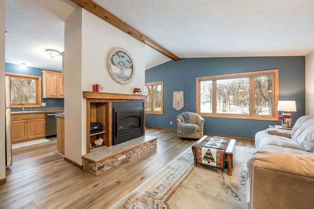 living room featuring sink, lofted ceiling with beams, a textured ceiling, and light wood-type flooring