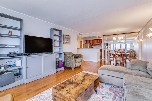 living room with a chandelier, built in shelves, and light hardwood / wood-style floors