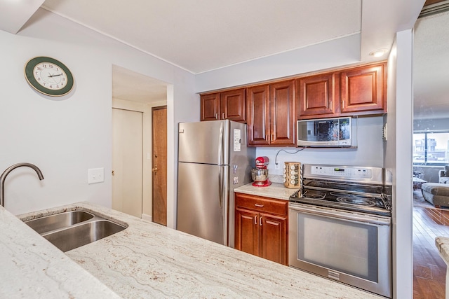 kitchen with light stone countertops, stainless steel appliances, hardwood / wood-style flooring, and sink