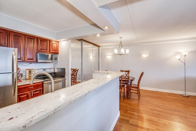 kitchen with light stone countertops, stainless steel appliances, light hardwood / wood-style flooring, a chandelier, and hanging light fixtures