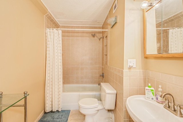 full bathroom featuring sink, tile patterned floors, a textured ceiling, toilet, and tile walls