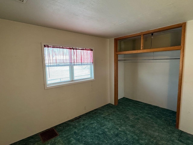 unfurnished bedroom with a textured ceiling, dark carpet, and a closet