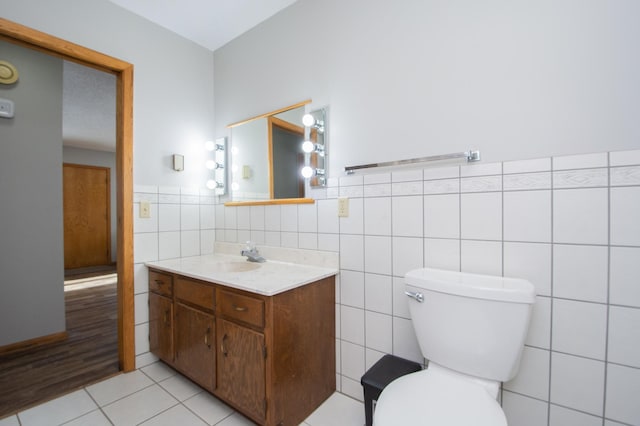 bathroom with toilet, vanity, tile patterned floors, and tile walls