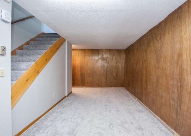 basement featuring wood walls, light colored carpet, and a textured ceiling