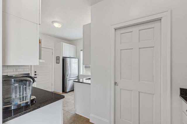 kitchen featuring stainless steel fridge, white cabinetry, dark stone countertops, tasteful backsplash, and light tile patterned flooring