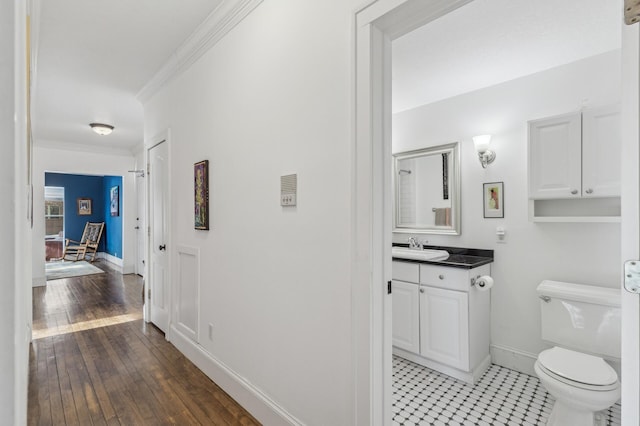 corridor with ornamental molding, a sink, light wood finished floors, and baseboards