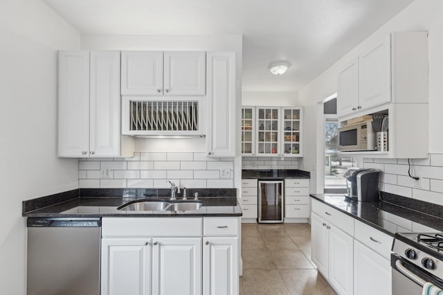 kitchen featuring beverage cooler, stainless steel appliances, a sink, white cabinetry, and tasteful backsplash