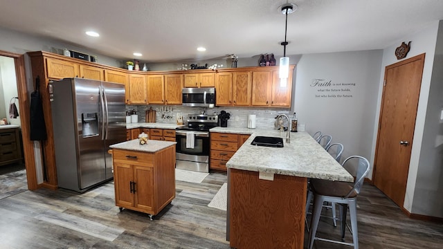 kitchen with a kitchen breakfast bar, stainless steel appliances, sink, a center island, and hanging light fixtures