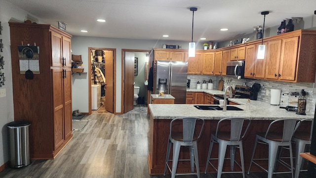 kitchen with backsplash, sink, hanging light fixtures, wood-type flooring, and stainless steel appliances