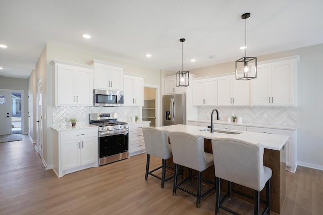 kitchen with a kitchen island with sink, white cabinets, appliances with stainless steel finishes, decorative light fixtures, and light hardwood / wood-style floors