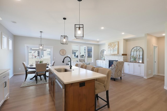 kitchen featuring sink, a stone fireplace, white cabinetry, and an island with sink