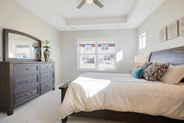 bedroom with ceiling fan, light carpet, and a tray ceiling