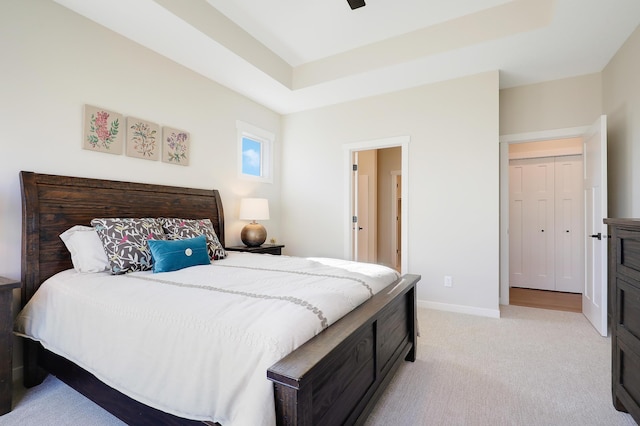 carpeted bedroom with ceiling fan, a raised ceiling, and a closet