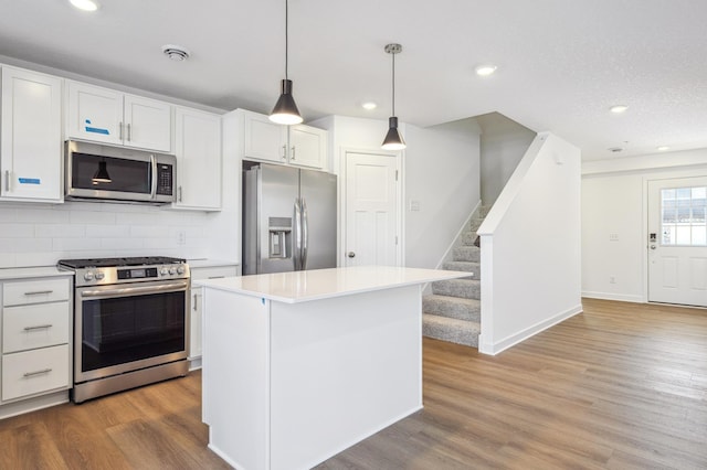 kitchen featuring white cabinets, hanging light fixtures, a center island, stainless steel appliances, and light hardwood / wood-style flooring