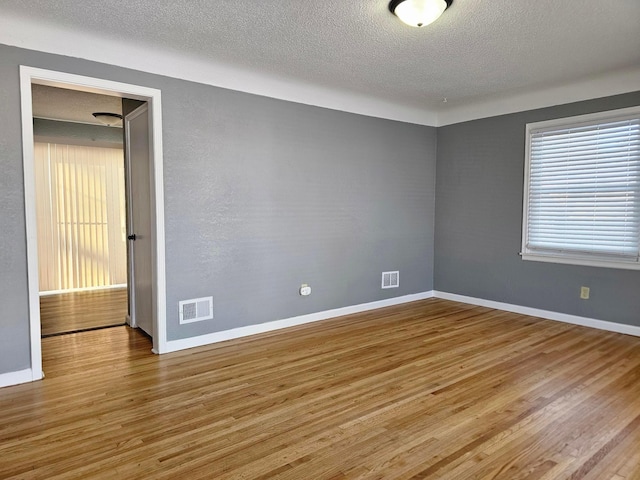 spare room with a textured ceiling and light hardwood / wood-style floors