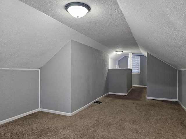 additional living space featuring lofted ceiling, a textured ceiling, and dark colored carpet