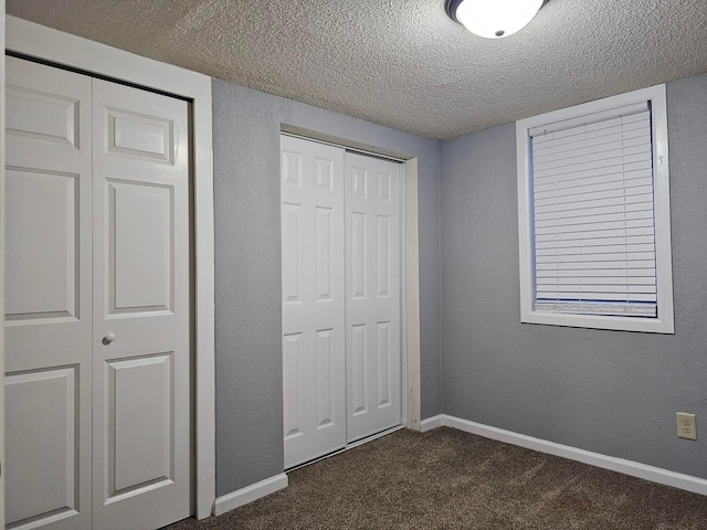 unfurnished bedroom with multiple closets, a textured ceiling, and dark colored carpet