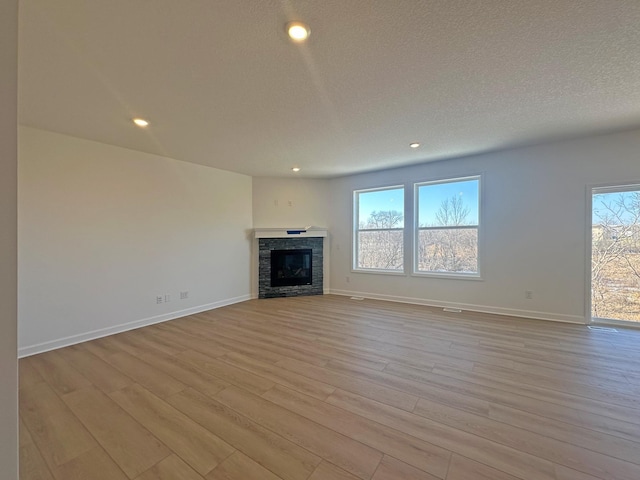 unfurnished living room featuring light wood-type flooring, a textured ceiling, and a fireplace