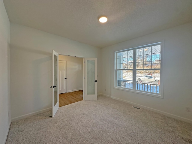 unfurnished bedroom featuring light carpet, a textured ceiling, and french doors