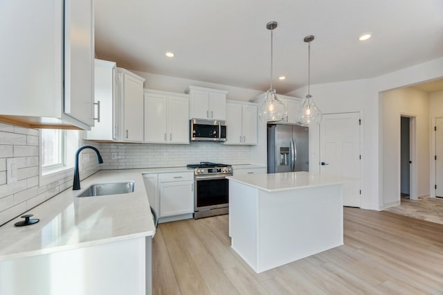 kitchen with white cabinets, appliances with stainless steel finishes, a kitchen island, decorative light fixtures, and sink