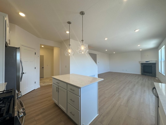 kitchen with pendant lighting, a center island, stainless steel refrigerator, light wood-type flooring, and a stone fireplace