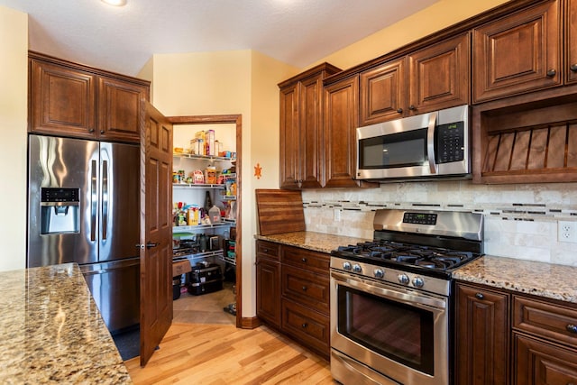 kitchen with stainless steel appliances, light wood-style flooring, decorative backsplash, and light stone countertops